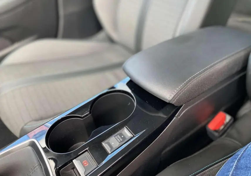 Gros plan sur la console centrale noire de la Peugeot 208 2021 avec accoudoir et commandes du frein à main électrique.
