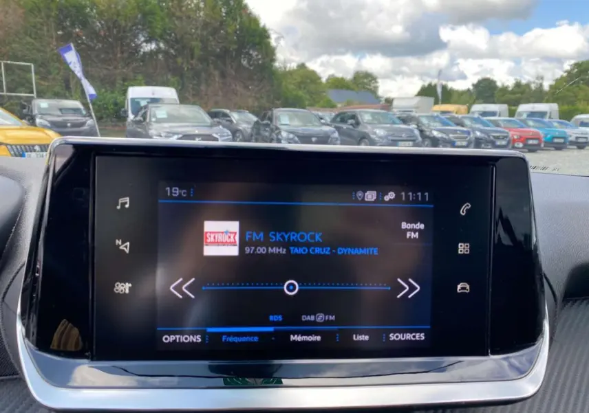 Écran tactile 7 pouces du tableau de bord de la Peugeot 208 noire, affichant la radio FM Skyrock en extérieur.