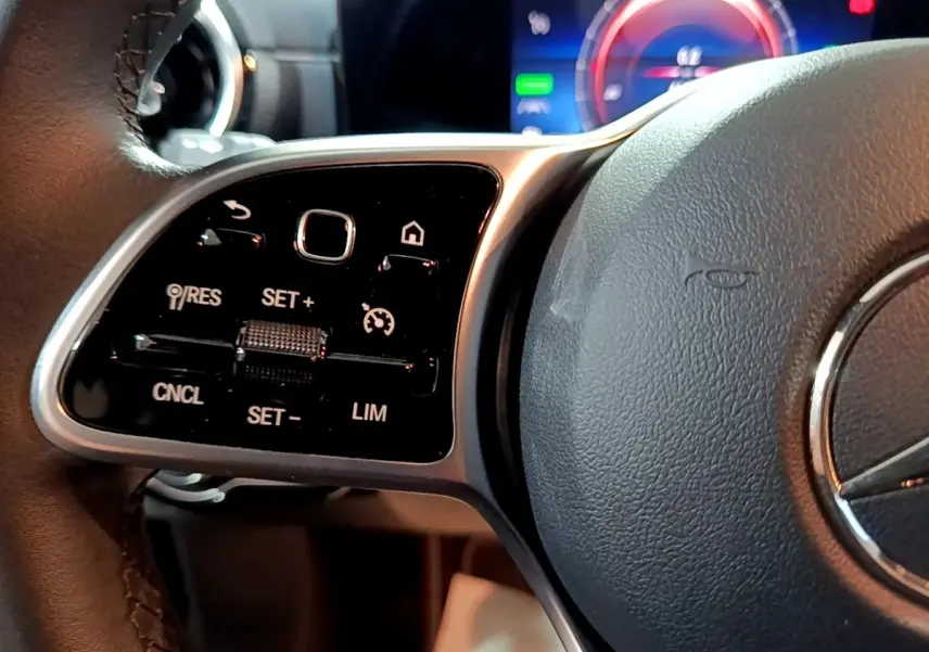 Gros plan sur le volant noir de la Mercedes Classe A 250 e, avec commandes multifonctions et affichage numérique en arrière-plan.