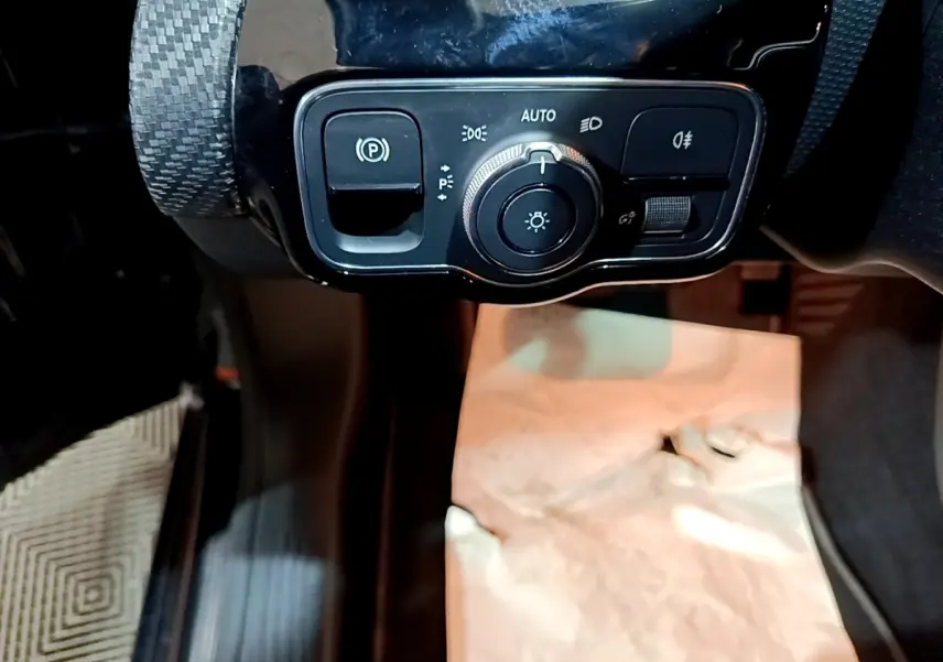 Gros plan sur le panneau de commande des phares et frein à main électrique dans l'habitacle noir d'une Mercedes Classe A 250 e.