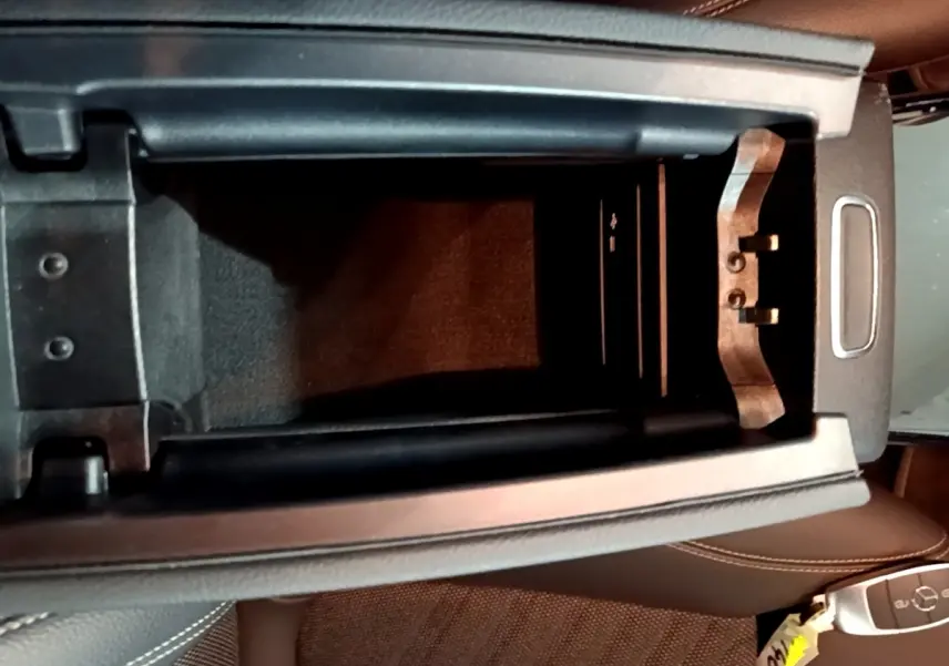 Vue plongeante sur l'accoudoir central ouvert et la clé Mercedes posée sur le siège en cuir marron.