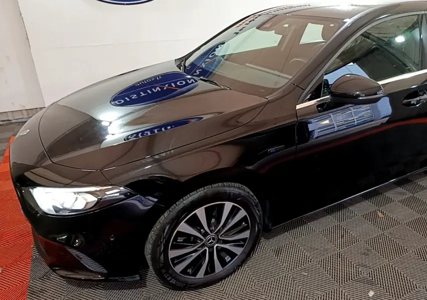 Vue 3/4 avant gauche d'une Mercedes Classe A 250 e Business Line noire avec jantes alliage et phares LED allumés.