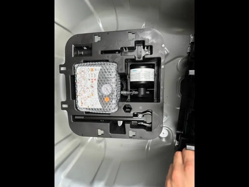 Vue rapprochée du kit de réparation de pneu dans le coffre gris Rafale d'une Renault Clio 2025.