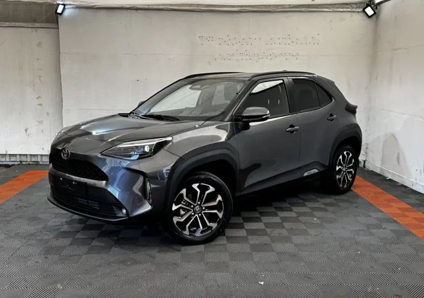 Toyota Yaris Cross 2026 gris foncé vue 3/4 avant avec jantes alliage et toit noir dans un garage.