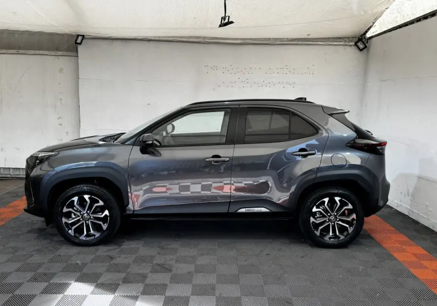 Profil droit de la Toyota Yaris Cross 2026 gris foncé avec jantes alliage et protections noires sur les passages de roues.