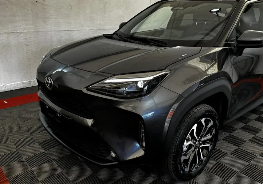 Vue 3/4 avant droit d'une Toyota Yaris Cross 1.5 Hybrid 130h gris foncé avec jantes alliage et phares LED allumés.