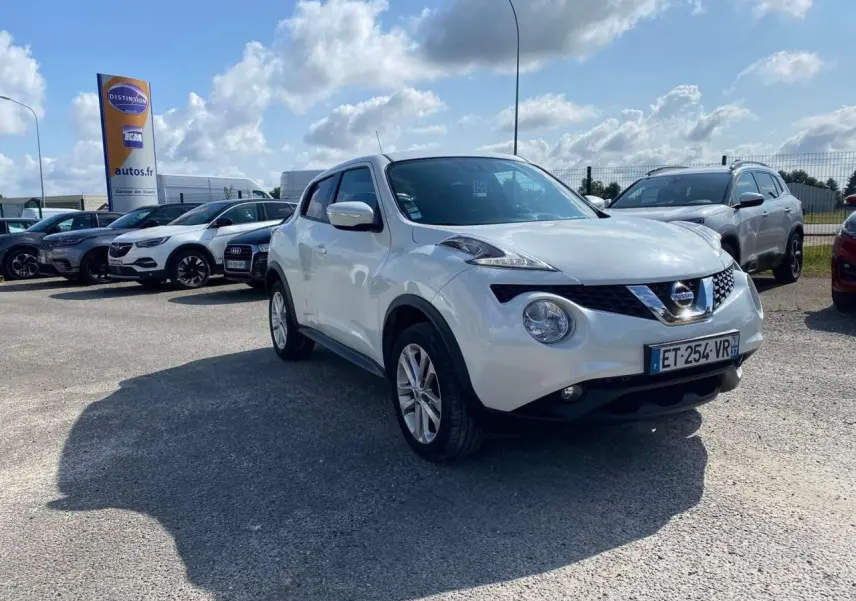 Nissan Juke blanc en 3/4 avant droit sur parking, avec jantes alliage 17 pouces sport visibles.