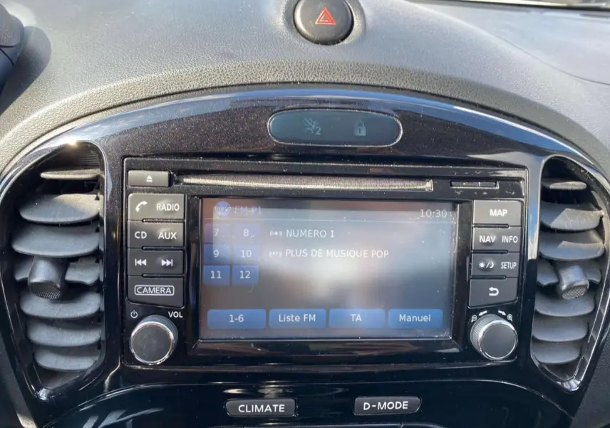 Vue rapprochée du tableau de bord noir du Nissan Juke avec écran tactile affichant la radio FM et commandes autour.