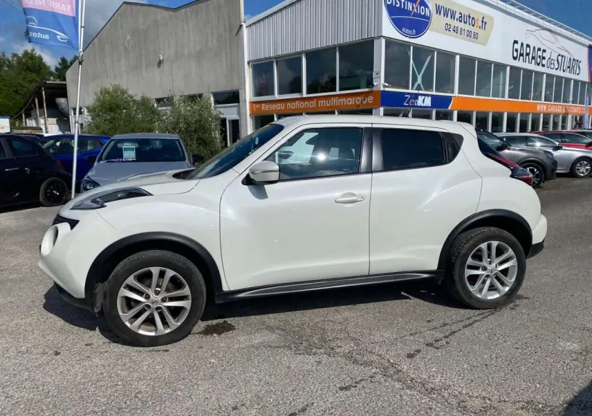 Profil côté gauche d'un Nissan Juke blanc 2017 avec jantes alliage 17 pouces, stationné devant un garage.