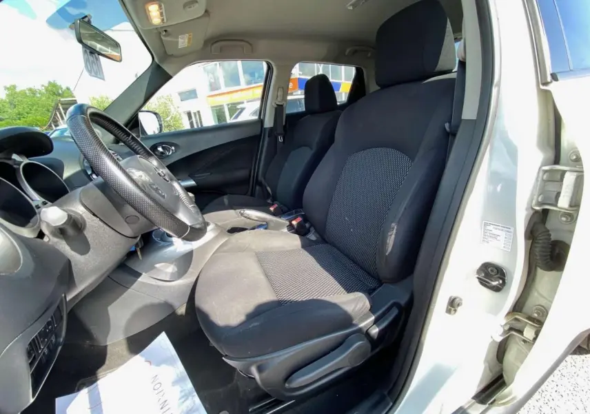 Vue intérieure côté conducteur du Nissan Juke blanc 2017 montrant les sièges noirs et le volant en cuir perforé.