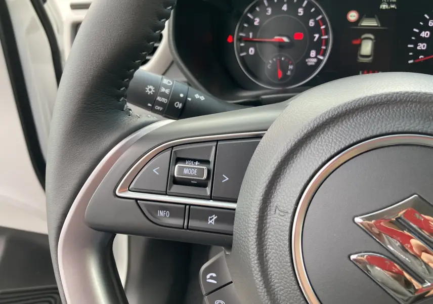 Gros plan sur le volant cuir multifonctions de la Suzuki Swift 2025, avec commandes audio et tableau de bord partiellement visible.