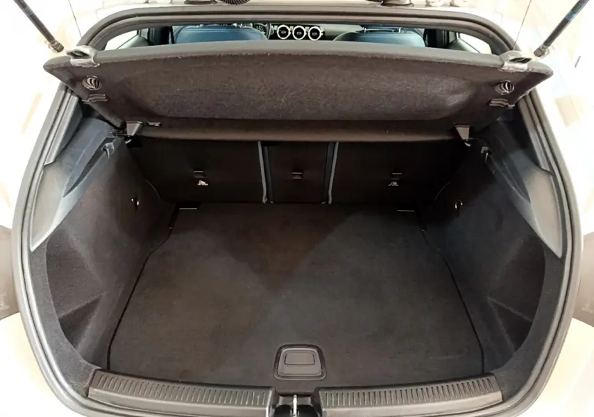 Coffre ouvert vu de l'arrière d'une Mercedes Classe A gris clair, montrant l'espace de chargement vide et la tablette de séparation.