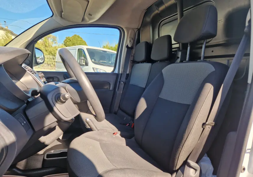 Vue intérieure côté conducteur du Renault Kangoo blanc 2021, montrant les sièges tissu noir et gris et le tableau de bord.