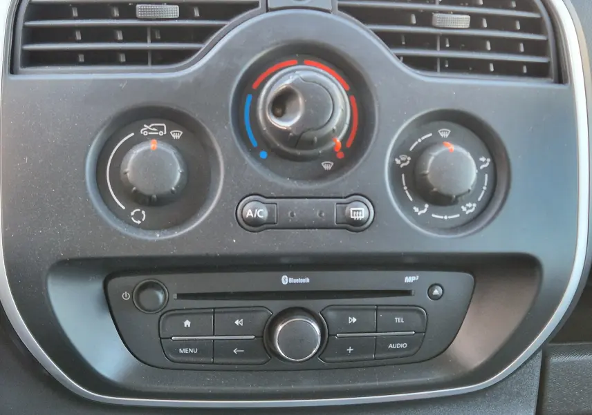 Détail du tableau de bord du Renault Kangoo blanc 2021, montrant les commandes de climatisation et la radio avec Bluetooth.