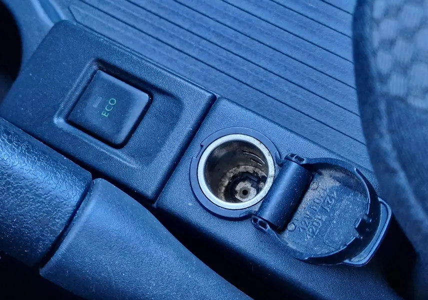 Gros plan sur la console centrale du Renault Kangoo blanc, montrant le bouton ECO et la prise allume-cigare ouverte.