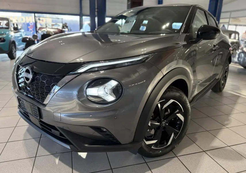 Nissan Juke Hybrid 143 N-Connecta gris métallisé en 3/4 avant droit avec jantes alliage noires et calandre en nid d'abeille.