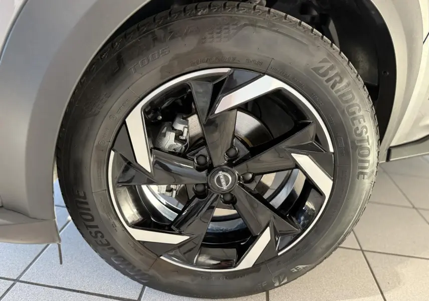 Gros plan sur la jante alliage 17 pouces noire et argentée du Nissan Juke Hybrid gris métallisé côté gauche.