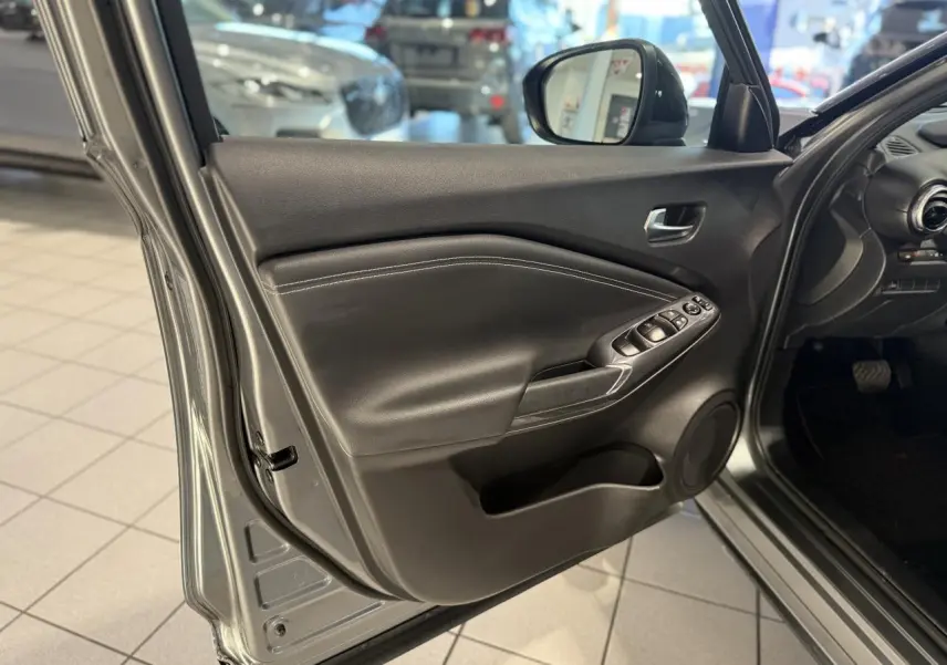 Vue rapprochée de la porte avant gauche gris métallisé du Nissan Juke Hybrid 143 N-Connecta avec commandes de vitres et haut-parleur intégré.