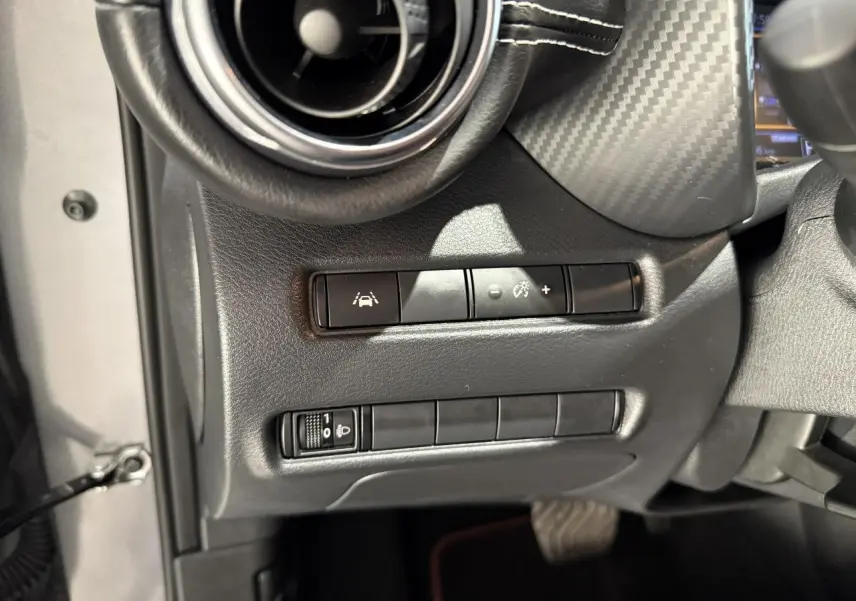 Gros plan sur les commandes d'aides à la conduite côté gauche du tableau de bord noir du Nissan Juke Hybrid 2024.