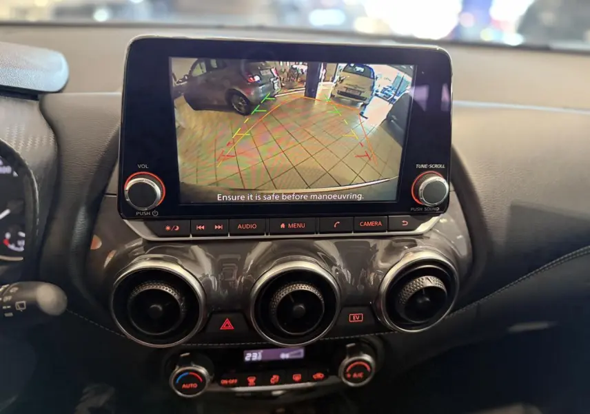 Vue rapprochée du tableau de bord du Nissan Juke Hybrid 2024 avec écran de caméra de recul et commandes de climatisation.