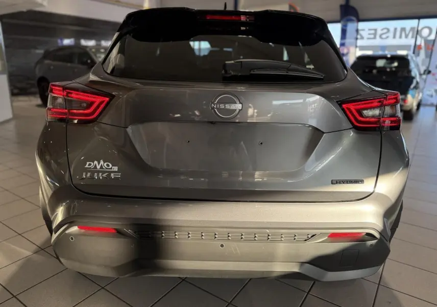 Vue arrière d'un Nissan Juke Hybrid gris métallisé avec feux arrière LED et logo Nissan visible en concession.
