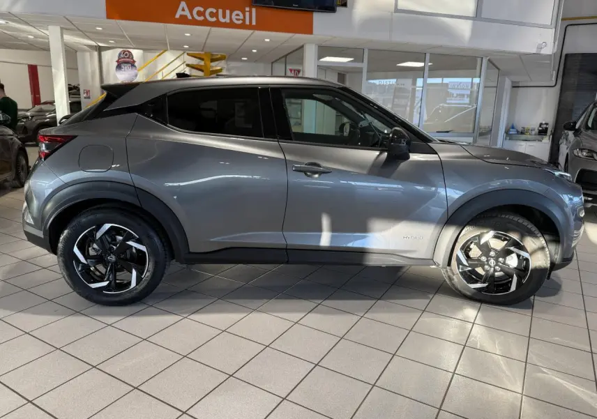 Profil côté gauche du Nissan Juke Hybrid 143 N-Connecta gris métallisé en showroom avec jantes alliage noires et chromées.