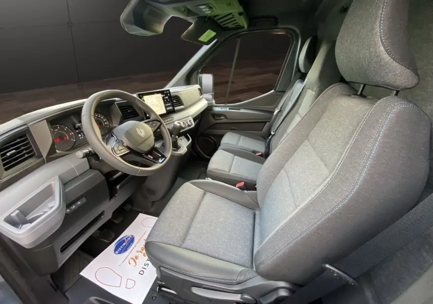 Vue intérieure côté conducteur du Renault Master 2025, montrant les sièges gris chiné avec surpiqûres bleues et le tableau de bord moderne.