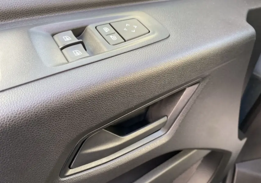 Gros plan sur la poignée intérieure et les commandes de lève-vitres côté conducteur du Renault Master gris urbain.