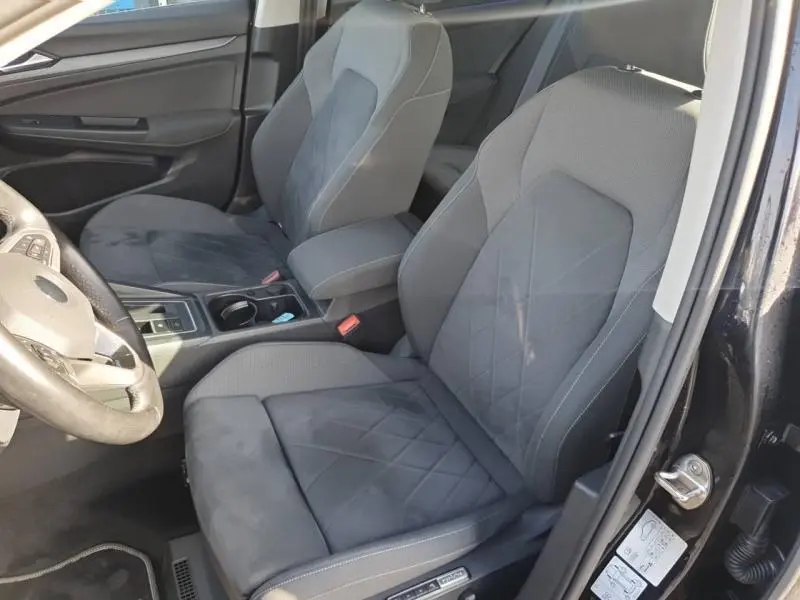 Vue intérieure côté conducteur de la Volkswagen Golf noire, sièges sport gris avec surpiqûres et accoudoir central.