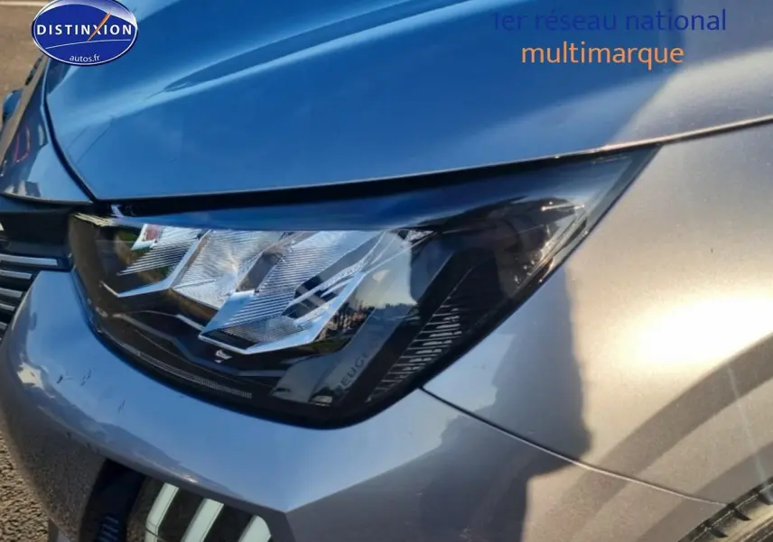 Gros plan sur le phare avant droit d'une Peugeot 208 gris artense avec reflets métalliques.