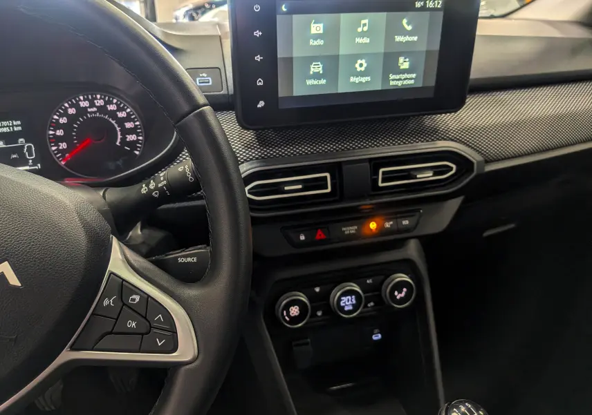 Vue intérieure côté conducteur du tableau de bord gris schiste de la Dacia Sandero 2025 avec écran tactile et commande manuelle.