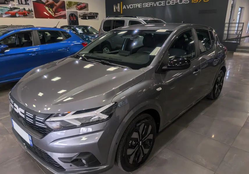 Vue 3/4 avant droite d'une Dacia Sandero TCe 90 gris schiste, avec jantes noires et rétroviseurs noirs brillants.