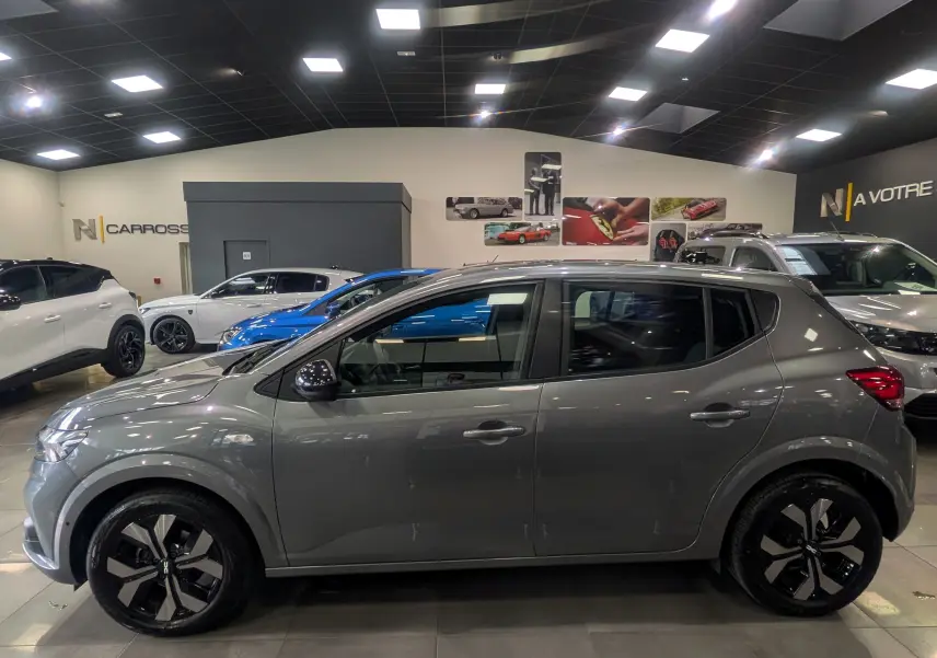 Profil côté gauche d'une Dacia Sandero TCe 90 CH Journey gris schiste, avec jantes noires et grises, en intérieur showroom.