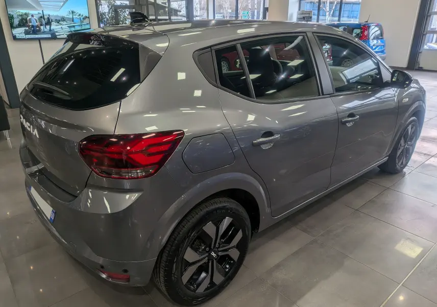 Vue 3/4 arrière droite d'une Dacia Sandero TCe 90 CH Journey 2025 en gris schiste, avec jantes alliage noires et vitres teintées.