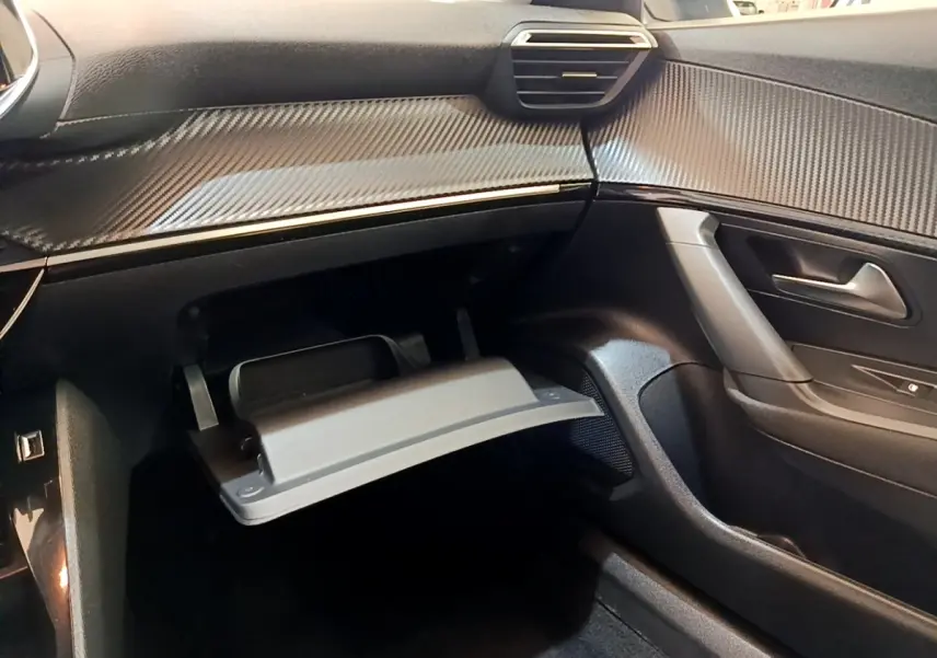 Intérieur noir de la Peugeot 2008, vue côté passager avec boîte à gants ouverte et tableau de bord effet carbone.