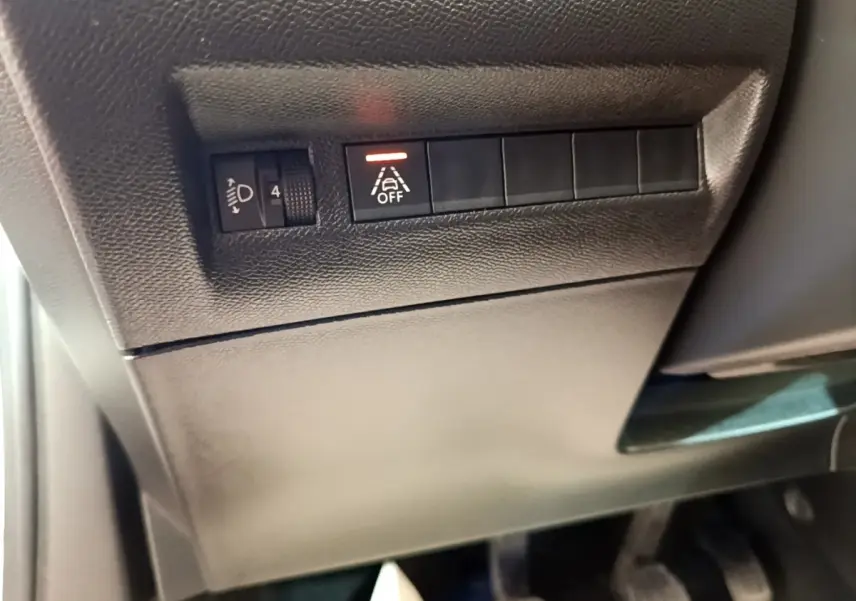 Détail du tableau de bord côté conducteur du Peugeot 2008 blanc, avec commande de réglage des phares et désactivation de l'alerte de franchissement de ligne.