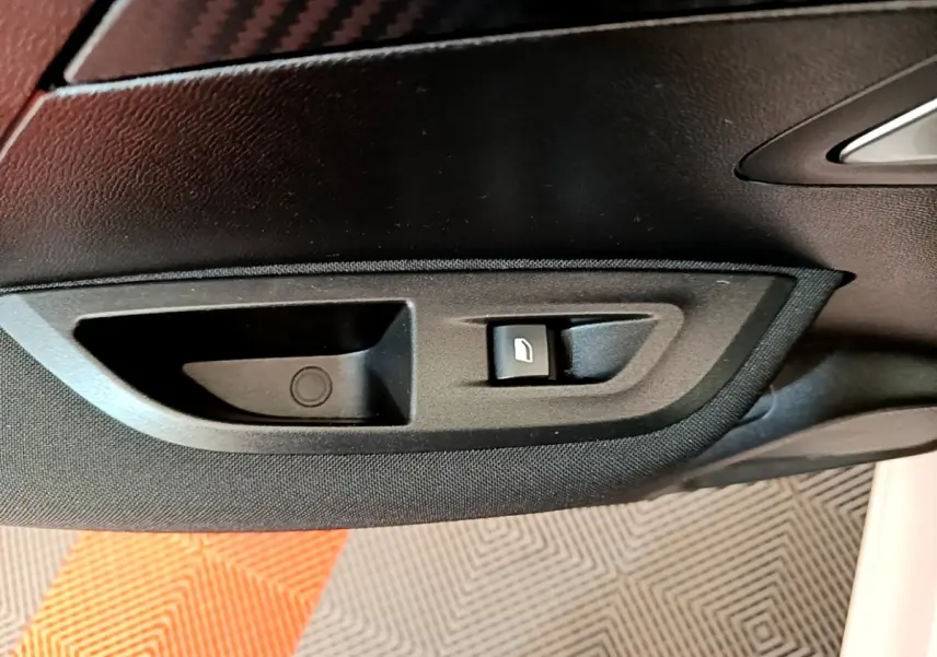 Gros plan sur la commande d’ouverture de coffre côté intérieur d’une Peugeot 2008 blanche, avec habillage noir.