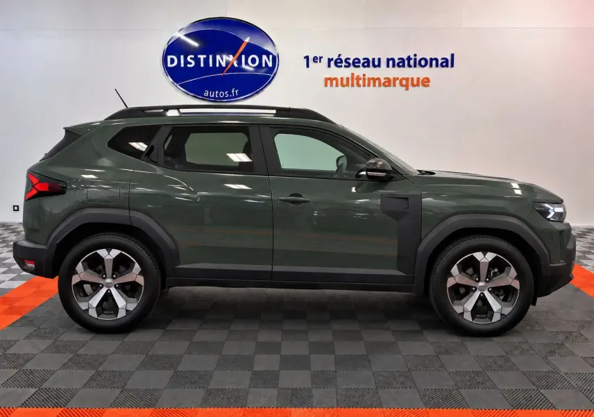 Profil latéral gauche du Dacia Duster 2026 vert cèdre avec jantes alliage et barres de toit noires.