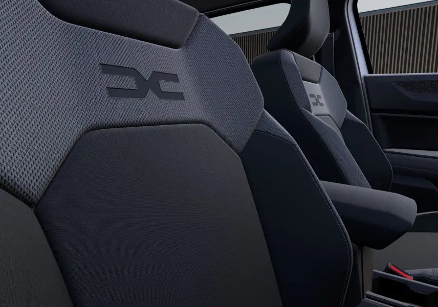 Gros plan sur les sièges avant en tissu gris foncé du Dacia Duster 2026 avec logo distinctif embossé.