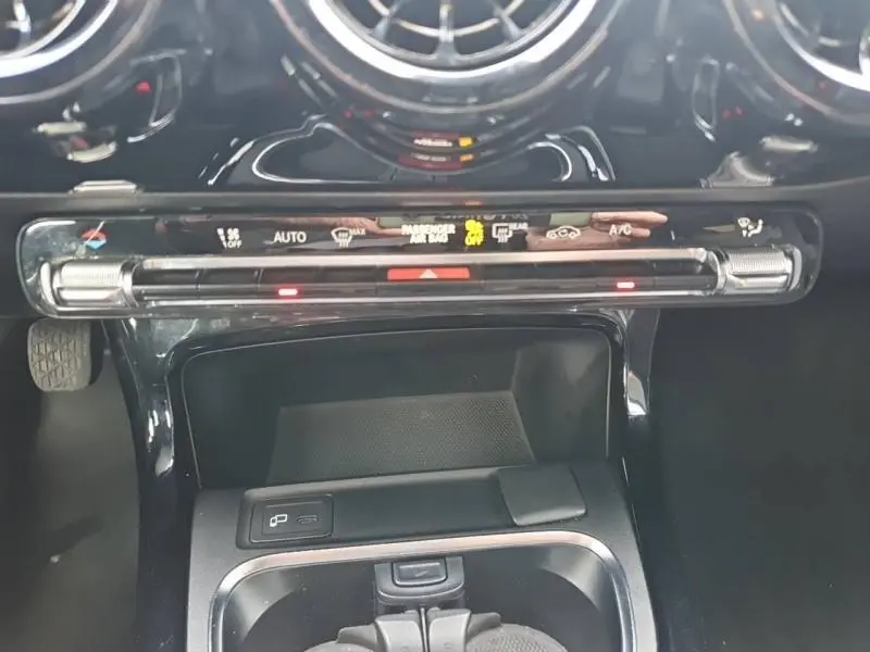 Vue rapprochée de la console centrale noire brillante avec commandes climatisation et aérateurs ronds d’une Mercedes Classe A gris montagne métallisé.