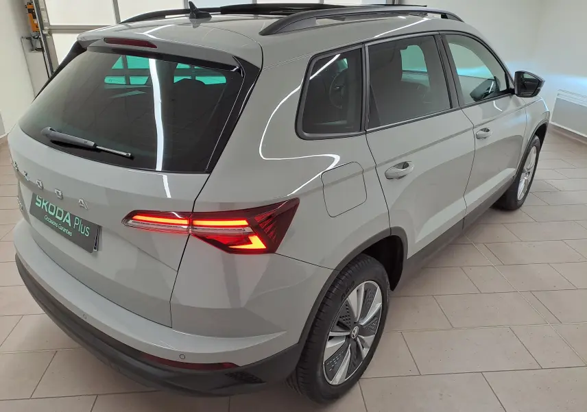 Vue 3/4 arrière droite du Skoda Karoq gris perle 2023 avec toit ouvrant panoramique et feux arrière allumés.