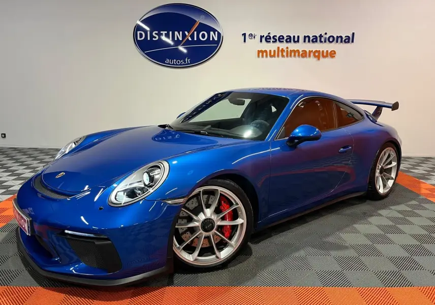 Porsche 911 GT3 bleu saphir en 3/4 avant droit, avec jantes sport et grand aileron arrière visible.