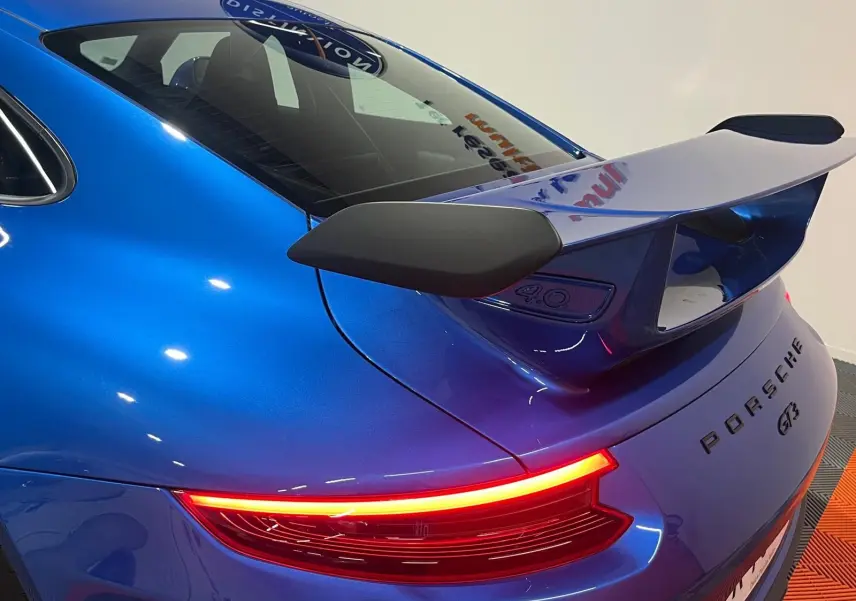 Vue 3/4 arrière droite d'une Porsche 911 GT3 bleu saphir avec aileron arrière et feux LED allumés.
