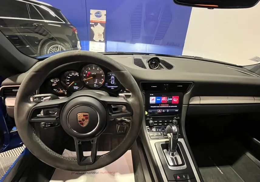 Vue intérieure centrée sur le volant sport alcantara et le tableau de bord de la Porsche 911 GT3 bleu saphir.