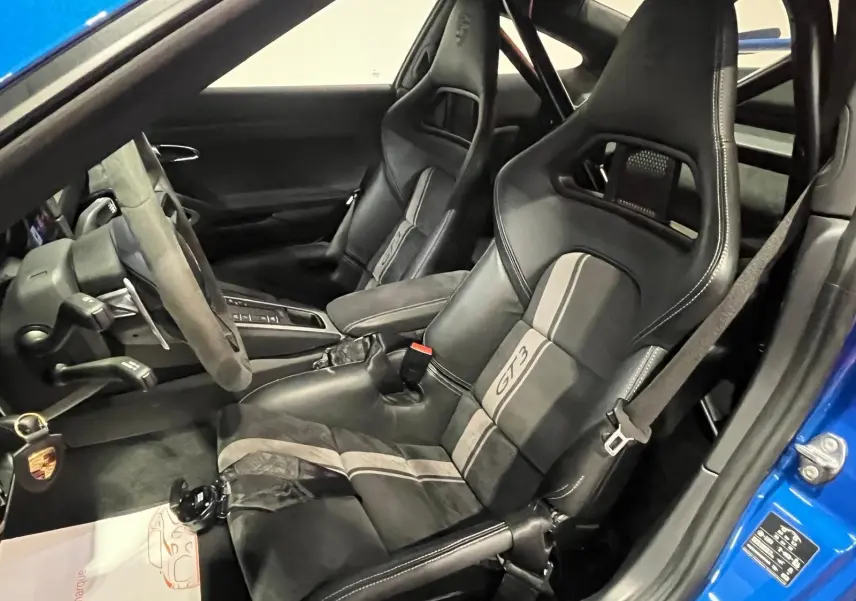 Vue intérieure côté conducteur de la Porsche 911 GT3 bleu saphir, avec sièges baquets sport et volant alcantara.