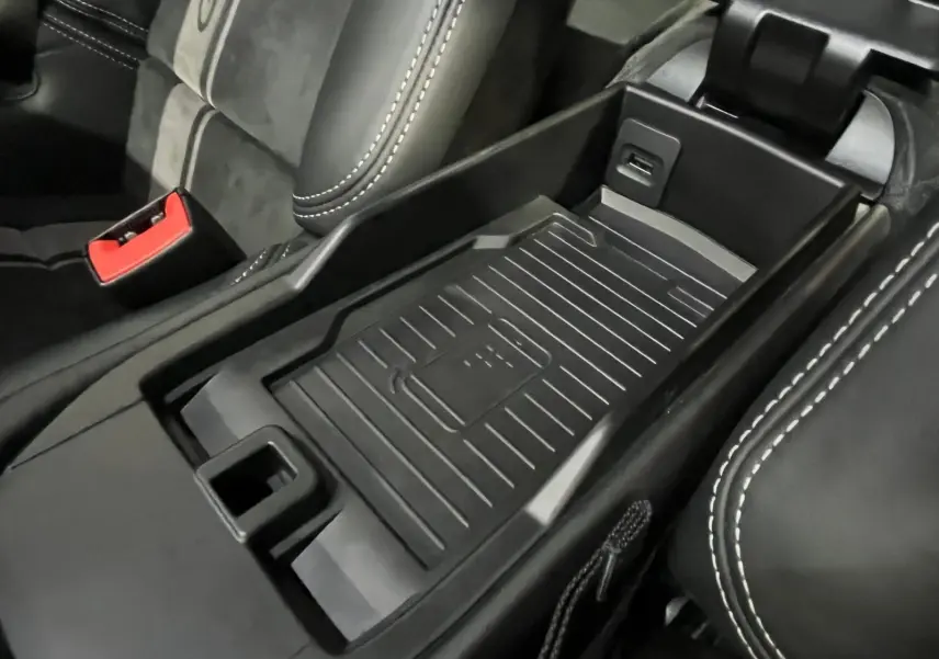 Gros plan sur la console centrale noire avec tapis antidérapant et surpiqûres blanches des sièges en cuir Alcantara.