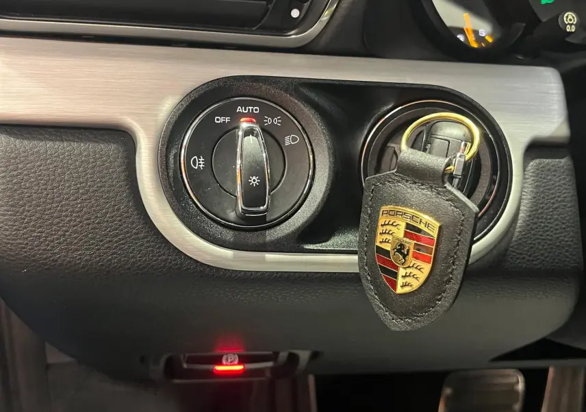 Détail intérieur montrant le contacteur d'éclairage et un porte-clés Porsche noir avec logo coloré.