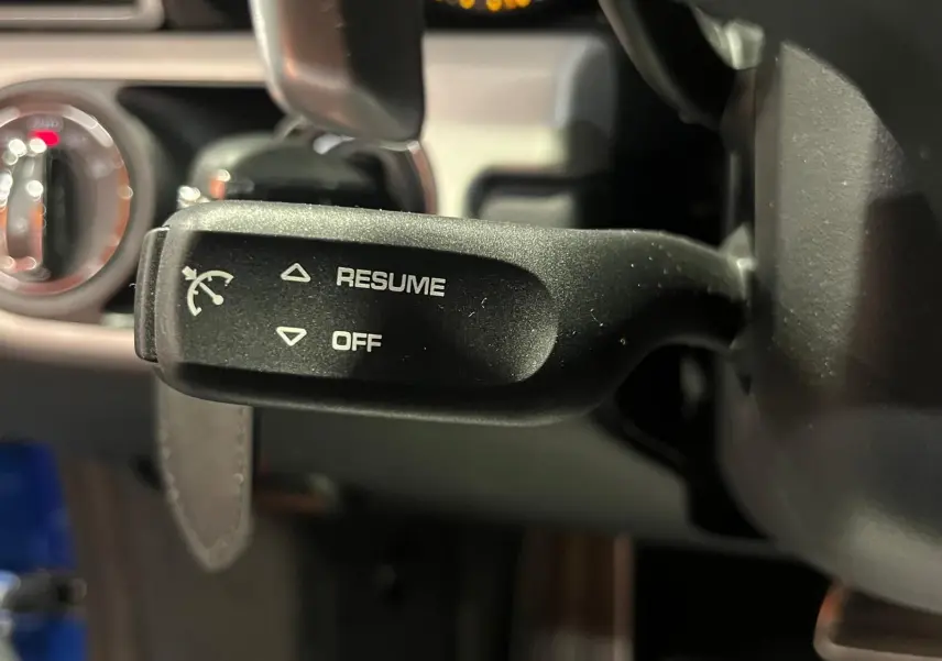 Gros plan sur la commande de régulateur de vitesse à gauche du volant dans l’habitacle d’une Porsche 911 GT3 bleu saphir.