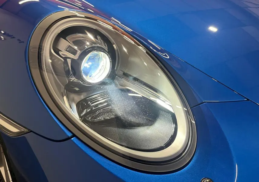 Gros plan sur le phare avant gauche d'une Porsche 911 GT3 bleu saphir brillant, soulignant ses détails modernes.
