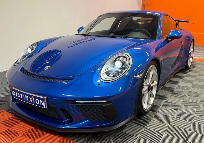 Porsche 911 GT3 bleu saphir vue 3/4 avant droit, avec jantes sport et aileron arrière visible.